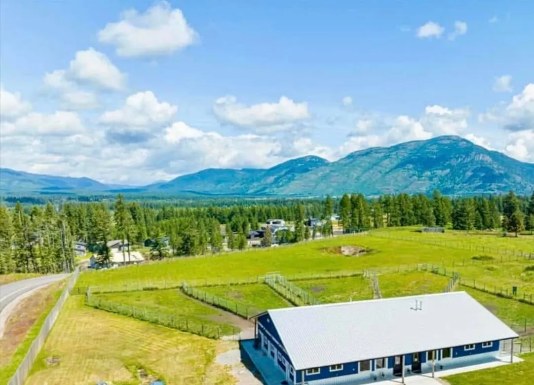 Aerial view of the blue ranch building and fenced yards at Columbia Mountain Dog Ranch, with mountains beyond.
