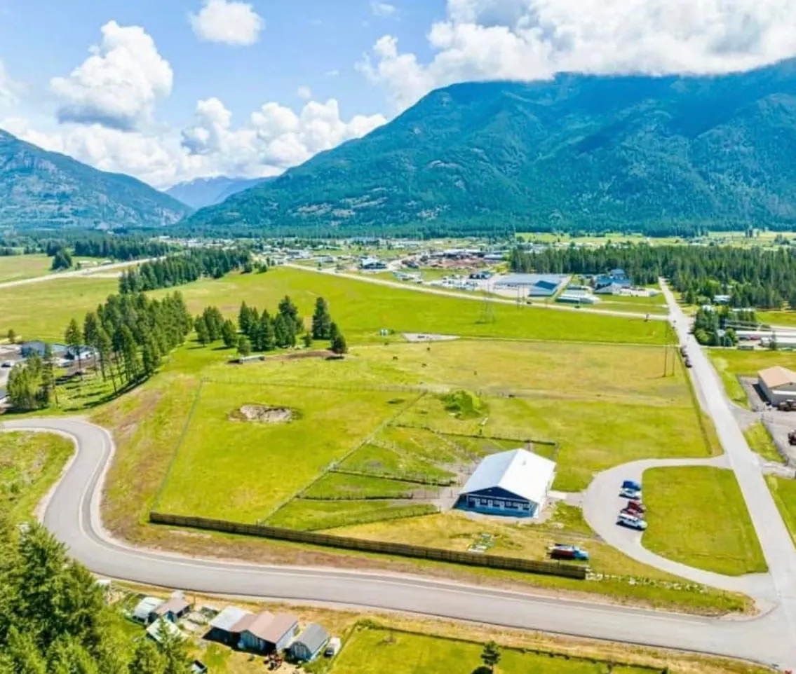 Aerial view of Columbia Mountain Dog Ranch, with the blue ranch building, fenced yards, and the Flathead Valley mountains beyond.